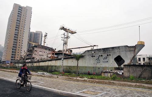 3月14日,一名男子從“古田”號旁騎行而過。在福建省福州市馬尾經濟開發(fā)區(qū)君竹路旁,有一艘擱淺了30多年的巨大水泥輪船——“古田”號,船體銹損嚴重,菜地遍布四周。如今,隨著城市開發(fā)建設,輪船所在地塊要進行征地,“古田”號的去留引發(fā)市民關注。據了解,這艘船是福州馬尾造船廠建造的迄今為止世界上最大的水泥船。1970年,馬尾造船廠承接了國家研制任務——造一艘載重量3000噸的水泥貨輪。1974年,鋼絲網水泥貨輪“古田”號成功下水。該船長105.2米,寬14.5米,深8.1米,吃水5.7米,排水量5773噸,適用于運送各類包裝貨和散裝貨。但該船因自重大、耗油量大,無法完成長途航運,在下水航行幾次后便停泊在港口。隨著歲月變遷,原來的水面早已成了陸地,只有它還擱淺于此。新華社發(fā)(張斌 攝)