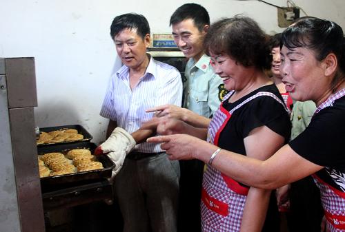 9月13日,在寧波市北侖區(qū)小港鎮(zhèn)陳山社區(qū)項(xiàng)金華阿姨家里,大伙開心地看著自己制作的月餅出爐。新華社發(fā)(索向魯 攝)