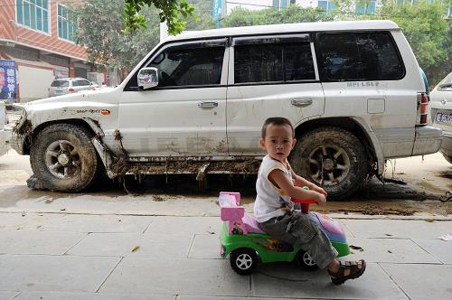 6月8日,望謨縣街頭,一個孩子騎著玩具車經過曾被洪水沖刷過的街道。 目前,貴州省、州、縣三級共籌集救災應急資金1400萬元下?lián)芙o望謨縣,截至7月7日16時,全省有解放軍、武警、消防、民兵、預備役人員1200人投入望謨抗洪搶險救災中。當?shù)厥転娜罕娬e極重建家園,恢復生活。 新華社記者 劉續(xù) 攝