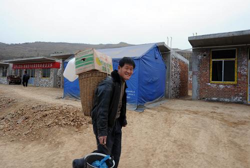 1月22日,隴南康縣豆坪鄉(xiāng)豆坪村一位村民背著年貨行走在新建的房屋前。 新華社記者 金良快 攝