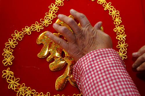 11月24日,在山東省郯城縣紅花鄉(xiāng)軒然工藝品廠,一位工人將“囍”字粘到中國(guó)結(jié)模版上。新華社記者 郭緒雷 攝