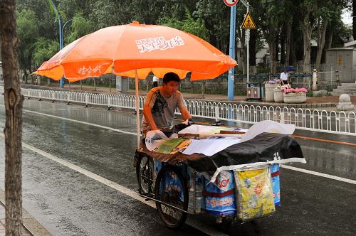 7月28日,長春街頭,一位冷飲攤主在雨中騎行。新華社發(fā)(張楠 攝)