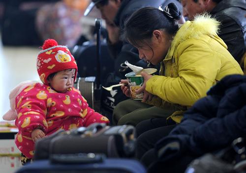 2月19日,來自安徽的一對母子在南昌火車站候車室等車間隙吃方便面,他們將乘坐1235次列車前往昆明。新華社記者 周科 攝