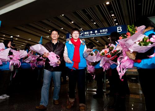 12月28日,來(lái)自印度尼西亞首都雅加達(dá)的游客尤利尤斯·韓(左)手捧鮮花在北京旅游志愿者的引領(lǐng)下走出首都國(guó)際機(jī)場(chǎng)的到達(dá)出口。新華社記者 張宇 攝
