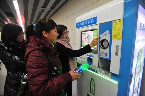 12月20日,在北京地鐵10號(hào)線芍藥居站,工作人員引導(dǎo)一名女乘客操作塑料飲料瓶智能回收機(jī)。新華社發(fā)(劉長龍 攝)