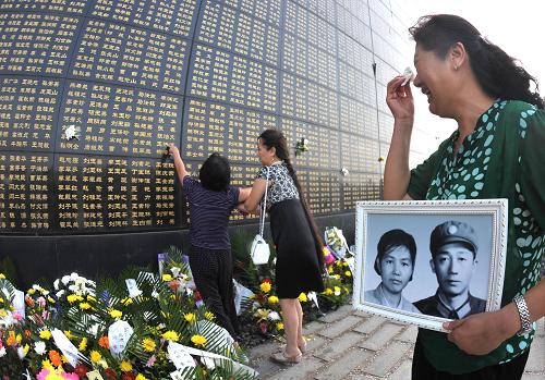 7月28日,一位女士手捧照片在紀(jì)念墻旁追思逝去的親人。新華社發(fā)(閆軍 攝)