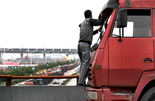 府谷至保德的大橋上因?yàn)槎萝?chē),一位司機(jī)下車(chē)擦車(chē)窗,橋下從忻保高速(忻州-保德)保德出口駛出的運(yùn)煤車(chē)在山西保德縣城里排起了長(zhǎng)龍(9月5日攝)。新華社記者 劉瀟 攝