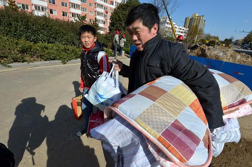 11月27日,一名學(xué)生家長(zhǎng)拿著孩子的被褥衣物,陪著孩子從青島開(kāi)發(fā)區(qū)第二中學(xué)走出。新華社記者 馮杰 攝