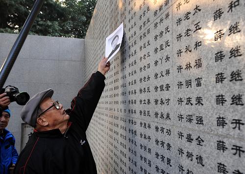 12月13日,南京大屠殺幸存者向遠(yuǎn)松拿著遇難親屬照片,在遇難者名單墻前祭拜。新華社記者 孫參 攝
