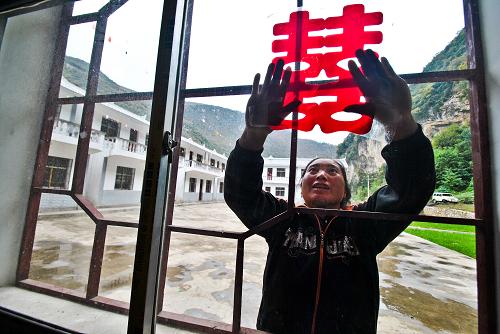 在貴州省威寧縣云貴鄉(xiāng)水塘村河邊組,一名村民在災(zāi)民安置點(diǎn)幫助準(zhǔn)備結(jié)婚的鄰居粘貼“喜”字窗花(2013年12月8日攝)。新華社發(fā)(楊文斌 攝)
