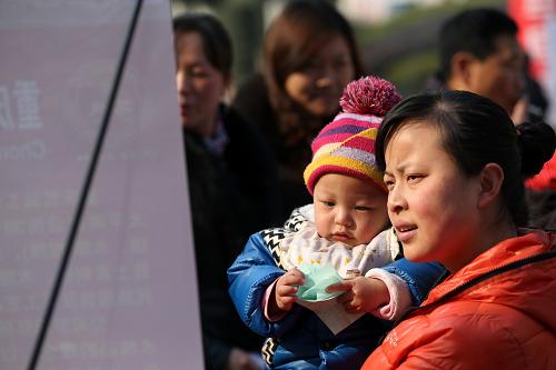 1月24日,一名媽媽帶著小孩在重慶市黔江區(qū)舉行的招聘會上查看招聘信息。新華社發(fā)(楊敏 攝)