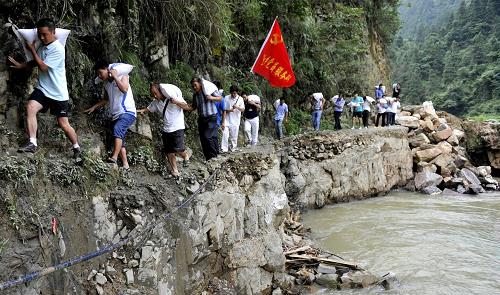 7月21日,黨員服務(wù)隊隊員背著大米等生活物資艱難走過被洪水沖斷的公路。新華社記者 歐東衢 攝