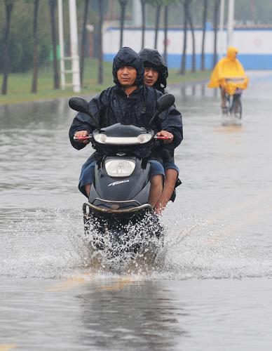 8月9日,市民騎電動車在積水路段上行進(jìn)。新華社發(fā)(沈鵬 攝)