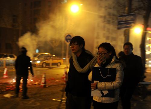 2月24日晚,北京東三環(huán)一小區(qū)外,一名行人用圍巾捂住口鼻,以躲避路旁燃放煙花產(chǎn)生的煙霧。新華社記者 羅曉光 攝