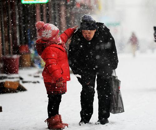 3月21日,在哈爾濱街頭,一名小朋友幫爺爺撲打身上的積雪。新華社記者 王凱 攝