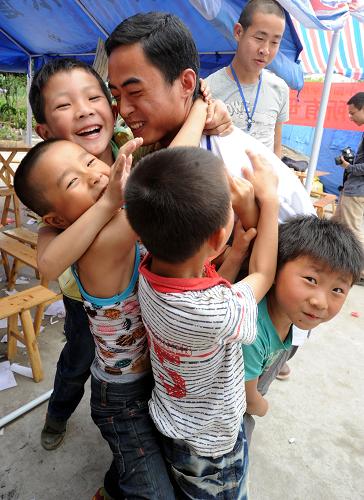 5月14日,在雅安市蘆山縣中國科學(xué)院心理研究所先鋒社區(qū)工作站的“心靈茶社”,幾名災(zāi)區(qū)兒童與一名心理援助志愿者嬉戲。新華社記者 李曉果 攝