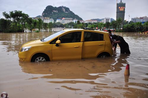 6月10日,在廣西柳州柳江路,市民在水中轉(zhuǎn)移汽車。新華社發(fā)(李書厚 攝)