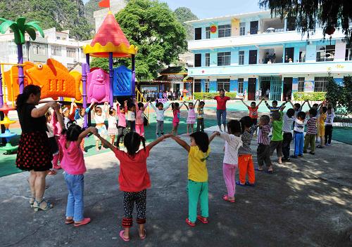 6月13日,在大化瑤族自治縣六也鄉(xiāng)中心幼兒園,小朋友們和老師一起做游戲。新華社記者張愛林?jǐn)z