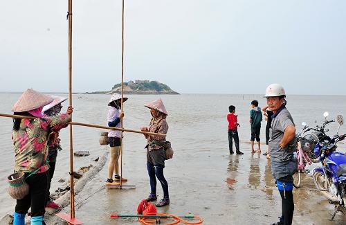 6月26日,村民正在跨海路口等待海水退潮后到草嶼島外面的灘涂上勞作。位于福建省莆田市北高鎮(zhèn)汀江村的草嶼島是一座孤島,四周環(huán)繞著近6000畝的養(yǎng)殖涂灘。“跨海路”未修之前,附近的村民到草嶼島周圍的涂灘勞作都要等到退潮后,趟著海水前往。從1999年3月開始,附近村民曾兩次自籌資金修建通往草嶼島的跨海道路,都被海水沖跨。今年2月,村民郭金通等又籌集了近200萬元資金,附近200多位村民自發(fā)開采石頭填海修路。經(jīng)過4個月的施工,這條600多米長的跨海路終于在5月底修建成功,為村民到灘涂上勞作提供了便利。新華社記者 林善傳 攝