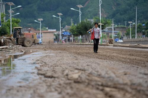 7月27日,一位扛著鐵锨的居民從被淤泥覆蓋的宜川縣云巖鎮(zhèn)街道上走過。新華社記者 李一博 攝