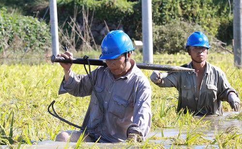 10月8日,國網(wǎng)永康市供電公司的搶修隊員扛著工具涉過齊腰深的積水。新華社發(fā)(徐芝婷 攝)