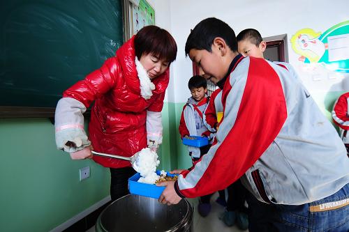 12月19日,西寧市城北區(qū)大堡子鎮(zhèn)小學(xué)教師賀宏燕(左)在給學(xué)生盛飯。新華社發(fā)(李少鵬 攝)