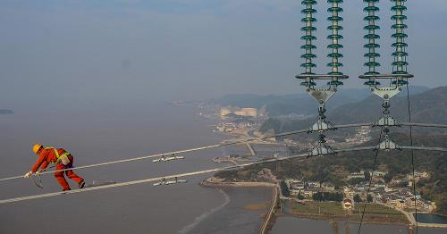 12月19日,浙江省送變電工程公司的施工人員在190多米高的電纜線上巡查。新華社記者 徐昱 攝