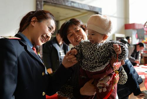 1月27日,蘭州火車站客運(yùn)員高子欽(左)向一位候車小朋友贈(zèng)送年俗掛飾。新華社記者 陳斌 攝
