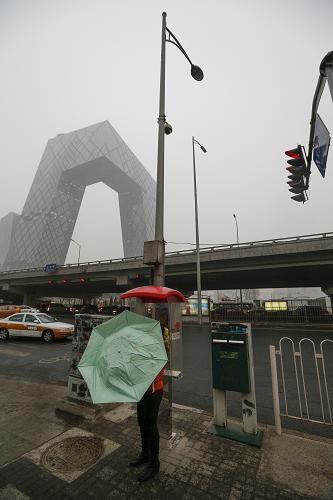 2月26日,在被霧霾籠罩的央視新址大樓附近,一名行人撐起雨傘擋雨。新華社記者 沈伯韓 攝