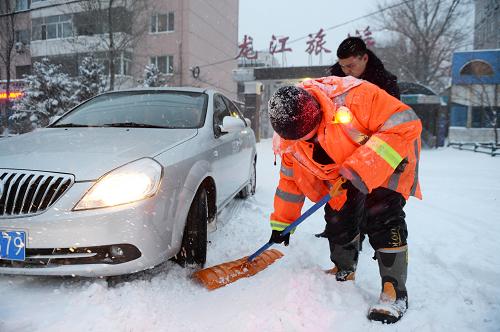 11月18日,一名哈爾濱市環(huán)衛(wèi)工人幫助一位私家車主鏟除車輪下的積雪。(新華社記者 王凱 攝)