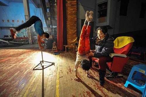 1月15日,中國重慶三峽雜技藝術(shù)團(tuán)的教練、老雜技演員周海燕(右一)在輔導(dǎo)學(xué)員練習(xí)雜技。早晨6點(diǎn)半,中國重慶三峽雜技藝術(shù)團(tuán)學(xué)員班的20多名孩子準(zhǔn)時出現(xiàn)在練功房里,軟功、劈叉、倒立……每項基本功都必須堅持至少30分鐘。雜技團(tuán)每年都會從三峽庫區(qū)各地招收一些愛好雜技的孩子進(jìn)行培訓(xùn)。“所謂‘臺上一分鐘,臺下十年功’,這些孩子一進(jìn)團(tuán)就要開始為期5年的基本功訓(xùn)練。學(xué)員排練一個好的節(jié)目,從熟練到上臺演出,需要花費(fèi)至少1年的時間。”青少年隊老師馮天桂告訴記者,能夠堅持到最后的學(xué)員不到70%。隨著社會的發(fā)展,就業(yè)渠道的多元化,這些年雜技在三峽庫區(qū)傳承顯得日趨艱難。為鼓勵學(xué)員全身心投入日常訓(xùn)練,雜技團(tuán)為學(xué)員提供食宿和穩(wěn)定的演出機(jī)會,并積極開拓國際市場,僅2013年就在美國進(jìn)行商演430多場次,全年共演出500多場次。成立半個世紀(jì)以來,三峽雜技團(tuán)培養(yǎng)出了許多優(yōu)秀的學(xué)員,他們出演的《雙人頂碗》《柔術(shù)滾杯》等一批雜技精品節(jié)目,在國內(nèi)外多次獲獎。新華社記者 劉潺 攝