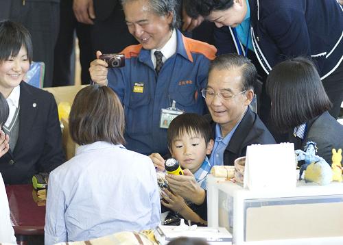 5月21日,中國國務(wù)院總理溫家寶在日本名取市館腰小學(xué)體育館災(zāi)民避難所慰問受災(zāi)民眾。這是溫家寶在教災(zāi)區(qū)小朋友使用中方贈送的應(yīng)急手電筒。 新華社記者黃敬文攝