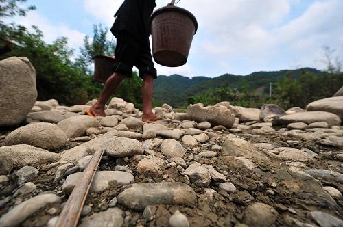 5月5日,在廣西田林縣八渡鄉(xiāng)八桃村,村民挑水從斷流的河床上走過(guò)。新華社記者 黃孝邦 攝