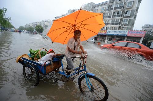 7月14日,江蘇揚(yáng)州遭暴雨襲擊,行人和車輛在街頭涉水而行。新華社發(fā)