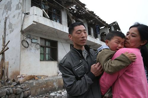 4月21日,在蘆山縣龍門鄉(xiāng)王家村,宋世勇一家在自家塌掉的樓房前。4月20日,四川雅安蘆山縣發(fā)生7.0級地震。截至21日9時25分,四川省雅安市蘆山縣7.0級地震共計造成179人死亡。新華社記者 金立旺 攝