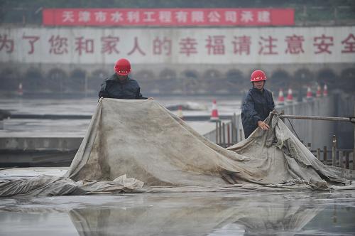 6月22日,兩名工人在工地現(xiàn)場苫蓋保護澆筑好的混凝土構(gòu)件。新華社記者 魯鵬 攝