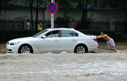 7月7日,一路人推著在水中熄火的汽車。新華社記者 程敏 攝