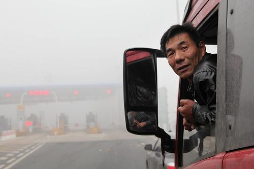 11月3日,車(chē)輛在長(zhǎng)深高速江蘇贛榆入口處排起“長(zhǎng)龍”,一名司機(jī)在駕駛室等待霧散放行。新華社發(fā)(司偉 攝)