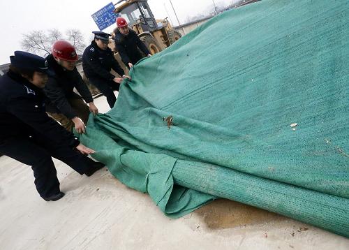 2月21日,執(zhí)法人員在一處工地內(nèi)對露天堆放的沙土進行遮蓋處理。 新華社記者 公磊 攝