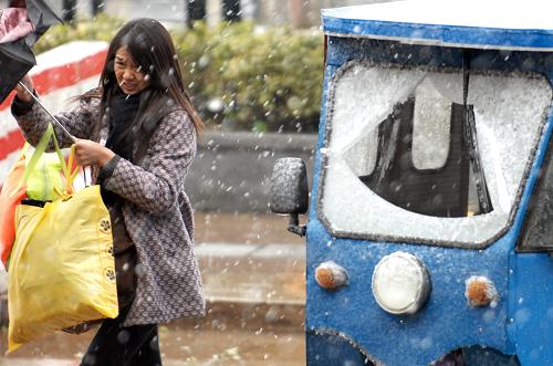 12月15日,在浙江衢州街頭,一位趕火車(chē)的旅客撐傘經(jīng)過(guò)被薄雪覆蓋的三輪車(chē)。新華社記者 鞠煥宗 攝