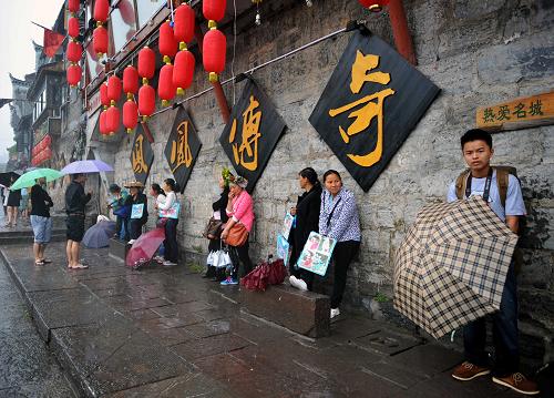 4月29日上午11時20分,一些游客和古城當?shù)氐木用穸阍谝粋€酒吧的屋檐下避雨。這些當?shù)鼐用褚詾橛慰团恼罩\生,一場降雨讓他們的生意更加清淡。4月29日,“五一”小長假的第一天,也是湖南省湘西土家族苗族自治州鳳凰古城實施148元“門票新政”后的首個小長假,上午和黃昏,兩場降雨給本來就因收費造成游客減少而備受非議的鳳凰古城新政帶來陰霾。記者深入鳳凰古城采訪時了解到,與往年“五一”假期游客爆棚的情形相比,今年的小長假有些“冷淡”,游客量不及往年的一半。鳳凰古城“門票新政”面臨第一次“大考”。但同時,鳳凰縣政府也在積極推出一系列被人們稱之為“補丁”的優(yōu)惠政策,以應對目前游客數(shù)量下降帶來的一些不良反應。“門票新政”何去何從?“鳳凰困局”如何化解?都引起社會輿論的高度高注。記者在不同地點和不同時段記錄下鳳凰古城在這個“五一”小長假的狀況。