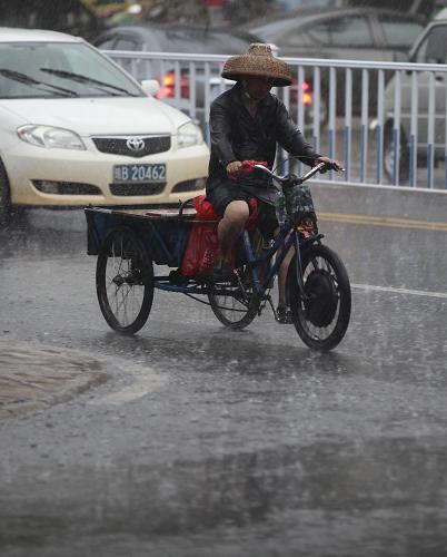 8月1日,在海南省三亞市街頭,市民在雨中騎行。 新華社發(fā)(陳文武 攝)