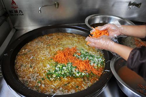 在寧夏固原市原州區(qū)張易鎮(zhèn)中心小學的食堂內,工作人員正在往學生的午餐里放胡蘿卜絲(6月13日攝)。
