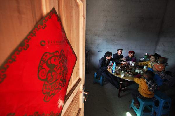 在重慶市黔江區(qū)太極鄉(xiāng)石槽村，村民徐超廷（左二）一家在新居吃農(nóng)歷除夕團(tuán)圓飯（2015年2月7日攝）。徐超廷左手殘疾，妻子多病，一家人靠兒子和兒媳在外打工維持生活。2014年，他家被納入精準(zhǔn)扶貧對象后，政府對他家進(jìn)行產(chǎn)業(yè)扶持，幫助其建起4畝獼猴桃園，并給予技術(shù)培訓(xùn)，使其成為了獼猴桃種植能手，實現(xiàn)了家庭增收。2015年2月，政府又對他家實施生態(tài)扶貧搬遷，幫助他修建了一棟兩層的小洋樓。同年底，徐超廷一家實現(xiàn)脫貧。